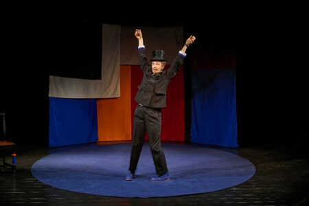 Anna Blomberg på scenen i kostym llyfter upp armarna.