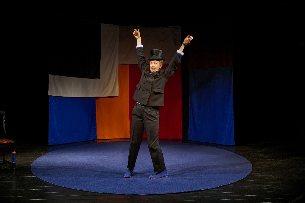 Anna Blomberg på scenen i kostym llyfter upp armarna.