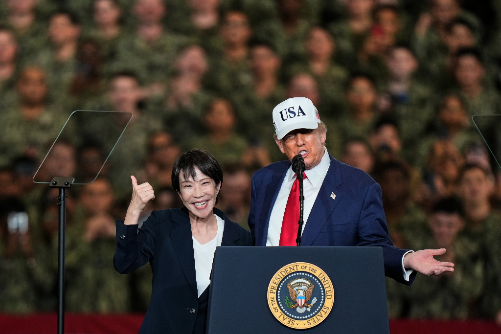 Sanae Takaichi och Donald Trump vid talarstol med soldater i bakgrunden.