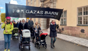 Demonstration med svart banderoll och flera barnvagnar.