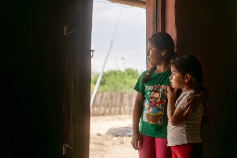 Två unga flickor tittar ut genom en dörröppning.