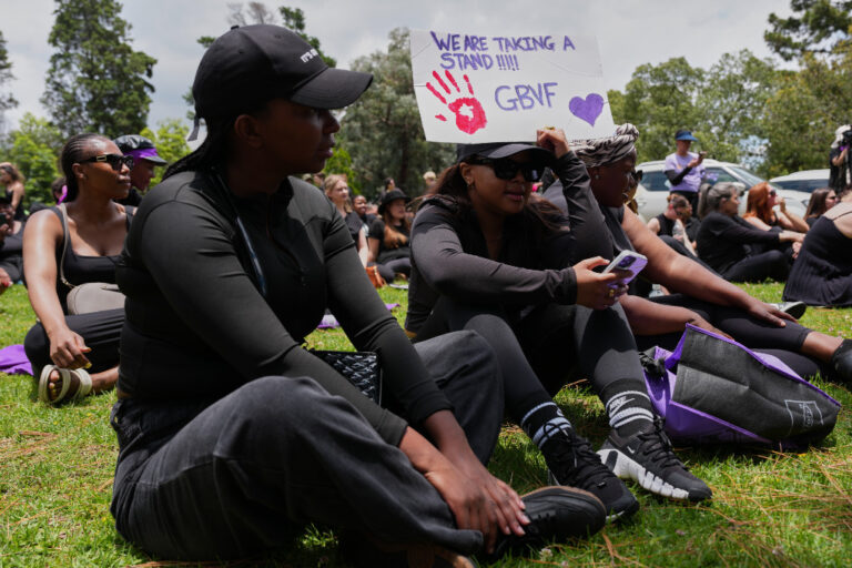 Demonstranter i svart sitter med plakat i hand.