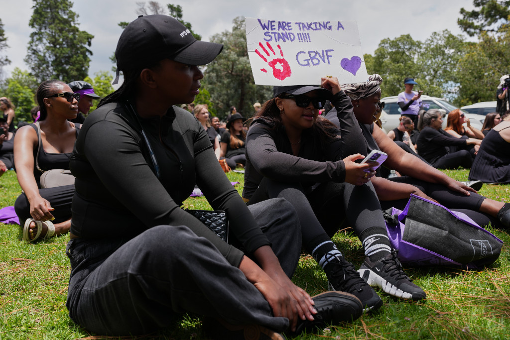 Demonstranter i svart sitter med plakat i hand.