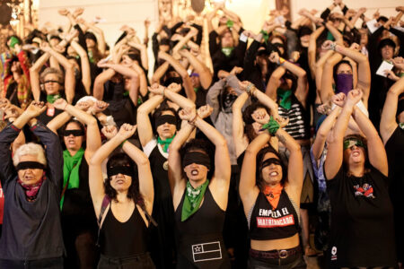 Kvinnor med bindel för ögonen håller upp armarna i kors under en demonstration.