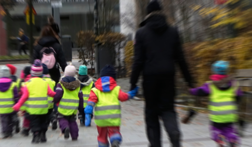 Förskolebarn iklädda gula reflexvästar går på en trottoar med en personal.