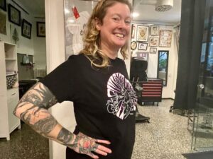 Sara Swanson i svart t-shirt ler och har tatueringar på armen.