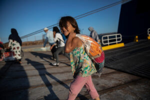 En leende flicka i rosa byxor bär påse på ryggen.