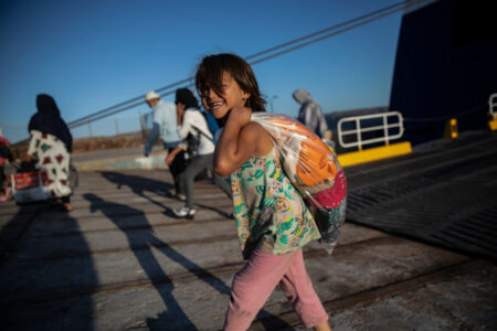 En leende flicka i rosa byxor bär påse på ryggen.